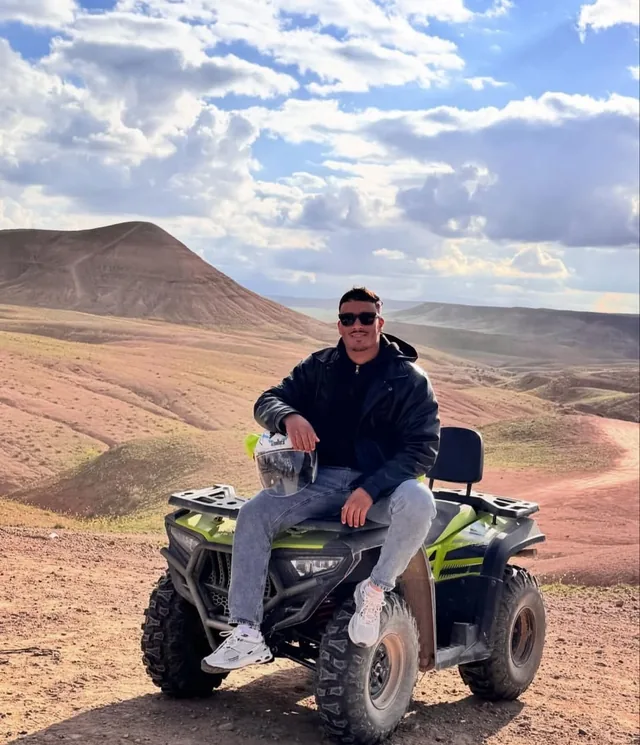 A rider sitting on a quad bike on an Agafay desert track with the stone hills and Atlas foothills behind