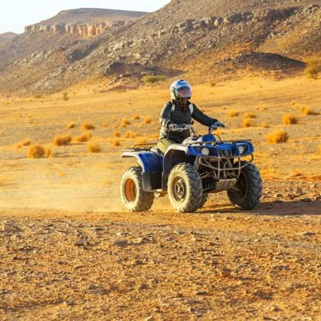 A helmeted quad rider on a desert piste below rocky hills