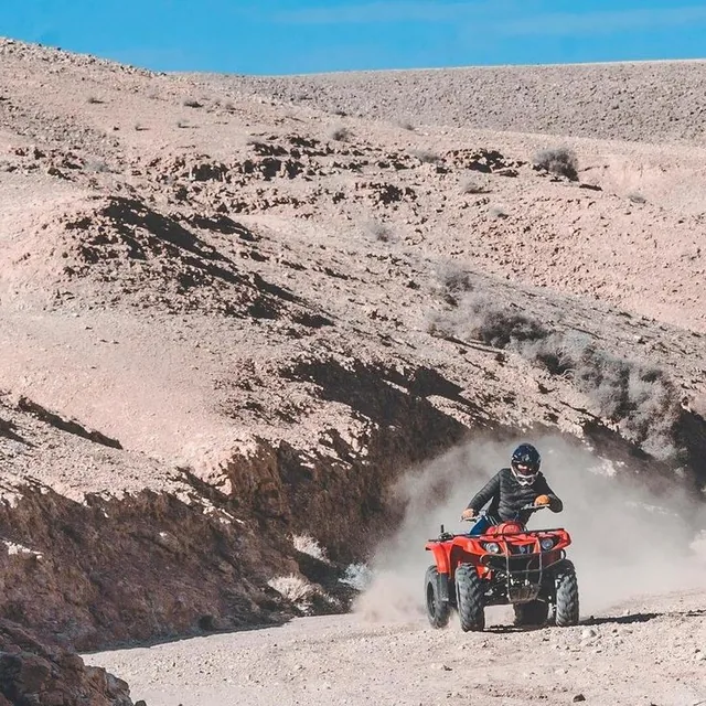 A red quad bike raising dust on a stony track through the pale Agafay hills