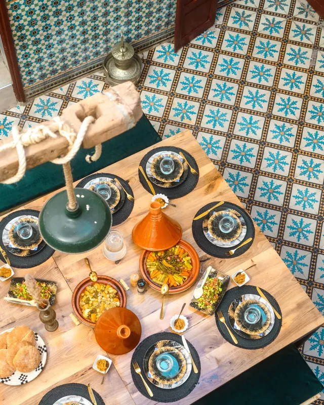 A long wooden table in a riad laid with tagines, salads and bread over patterned zellige tiles