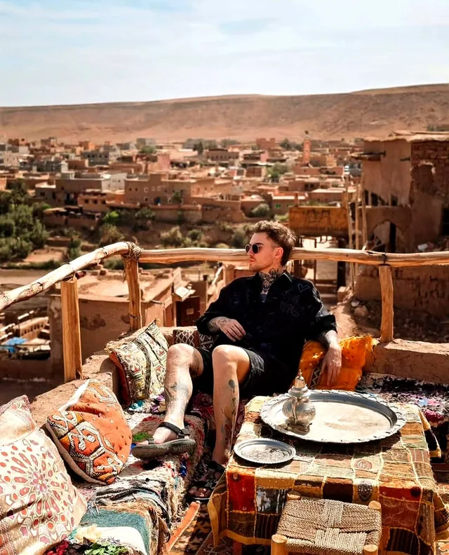 A traveller resting with mint tea on a rug-covered rooftop terrace overlooking a kasbah village