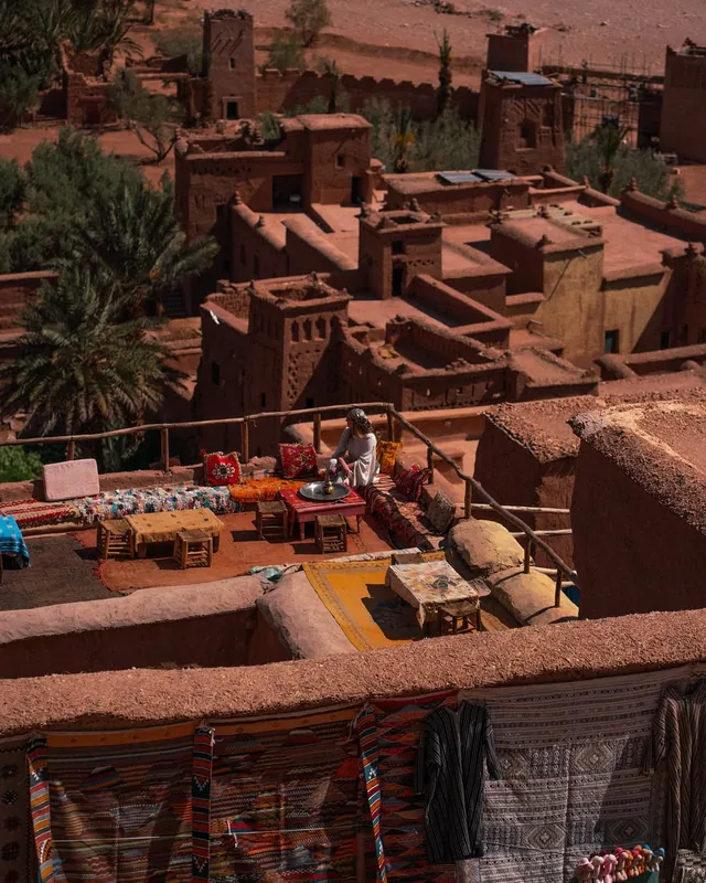 A rooftop tea terrace with low tables and rugs looking over the kasbahs of Aït Ben Haddou