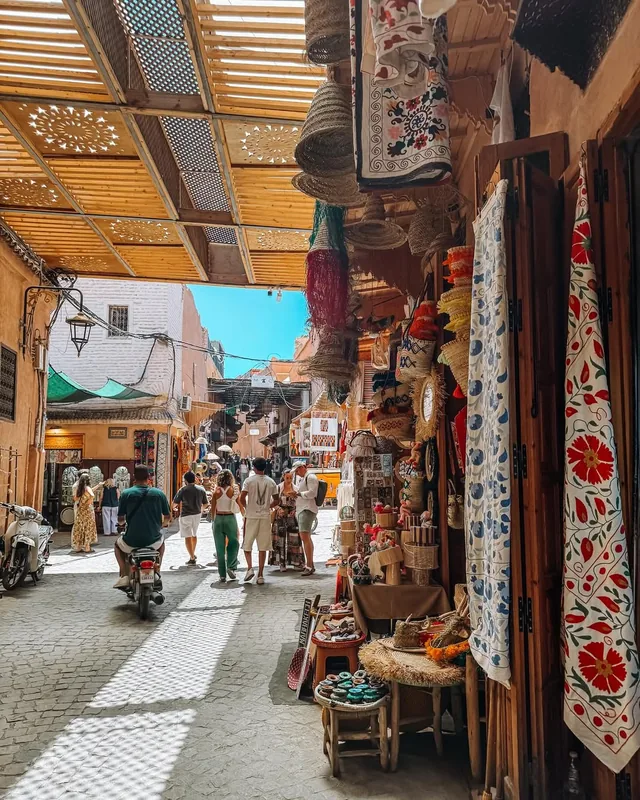A shaded Marrakech souk lane hung with woven baskets, lamps and embroidered textiles
