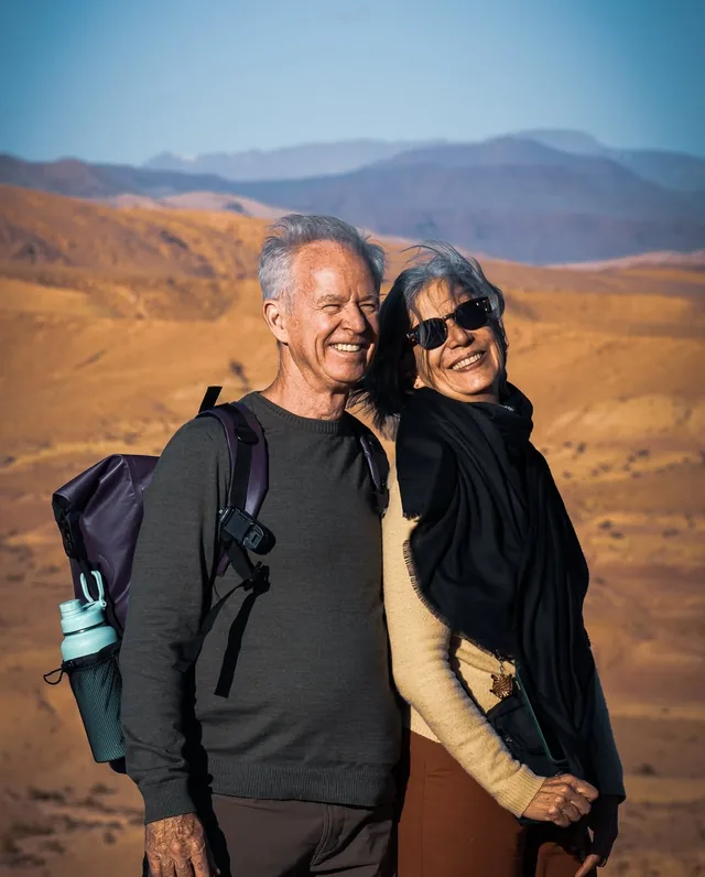 A smiling couple with daypacks at a desert viewpoint in southern Morocco