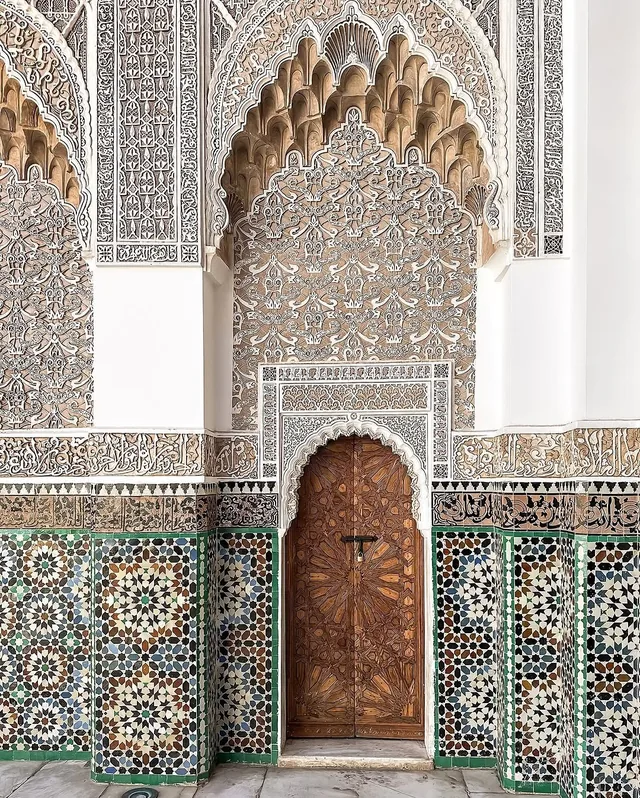 Detailed stucco carving and star-pattern zellige around a doorway at Medersa Ben Youssef