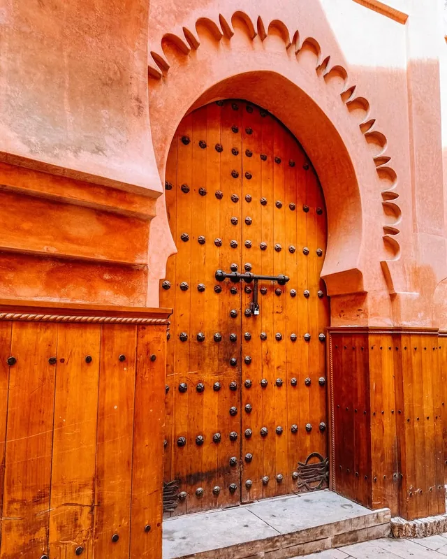 A studded wooden door set in a pink keyhole arch on a Marrakech medina street