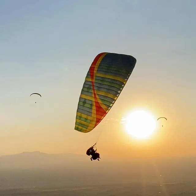 A tandem paraglider silhouetted against the setting sun above the Marrakech plain