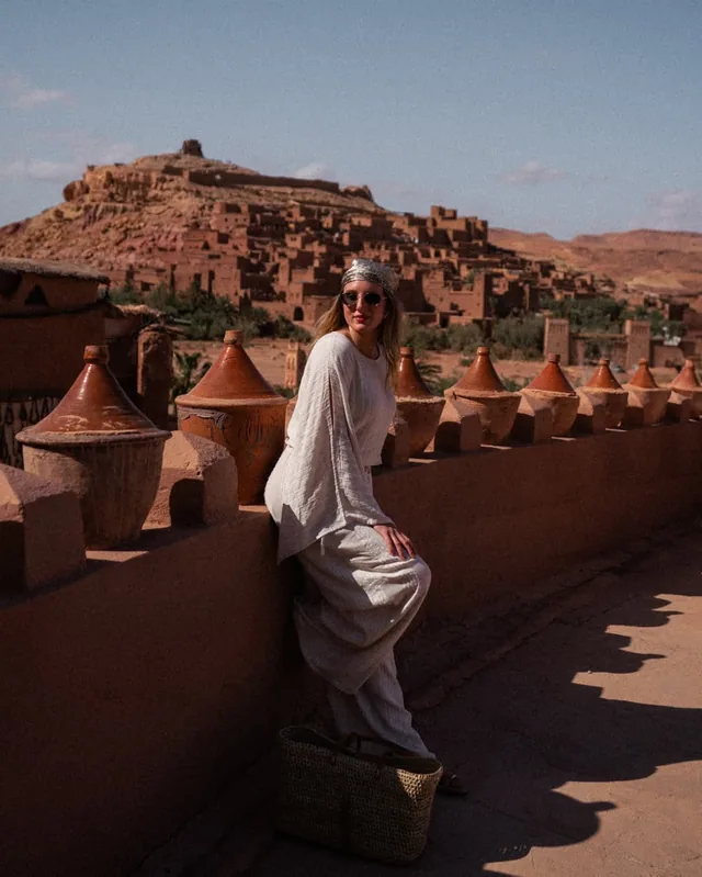 A traveller on a terrace lined with clay tagine pots facing the Aït Ben Haddou ksar
