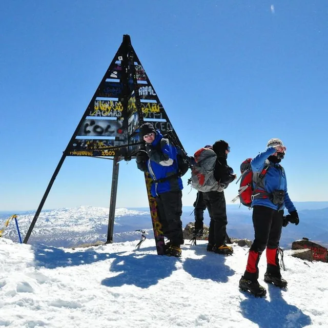 Climbers in crampons and gaiters beside the Toubkal summit pyramid above a snow-covered High Atlas panorama