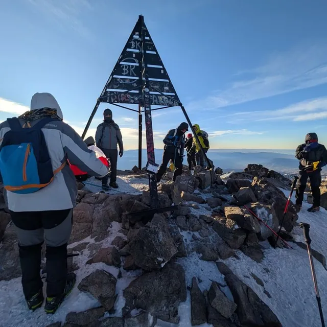 Trekkers gathered at the metal pyramid marking the summit of Mount Toubkal on a cold clear morning