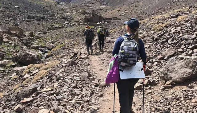 Trekkers walking the stony path up the valley towards a High Atlas mountain refuge