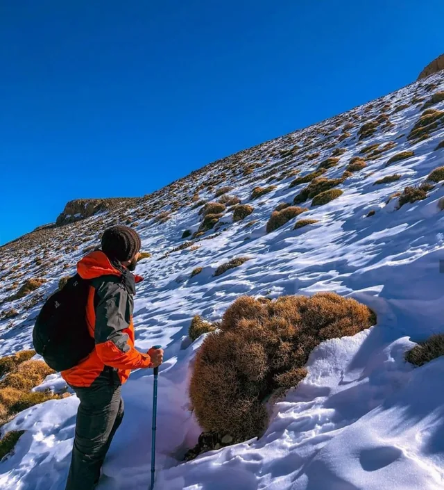 Wanderer mit Trekkingstöcken besteigt einen schneebedeckten Hang im Hohen Atlas