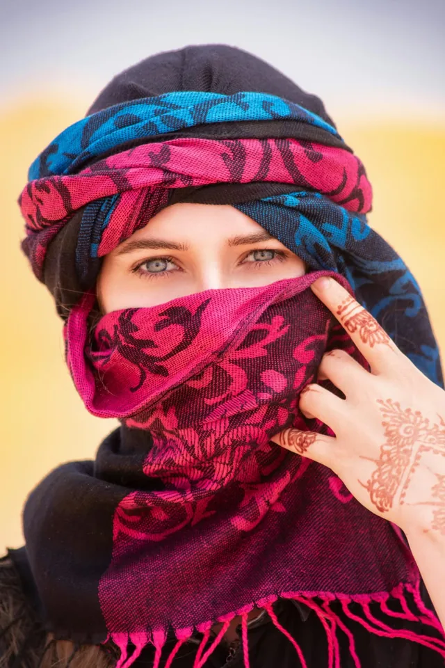 A traveller wearing a pink and blue desert turban, henna patterns drawn across her hand