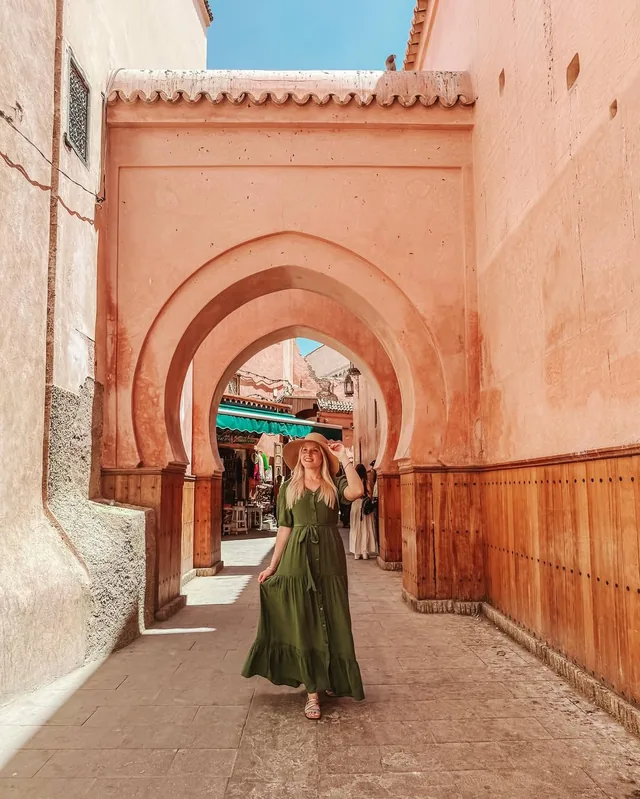 A traveller in a green dress standing under a pink horseshoe archway in the Marrakech medina