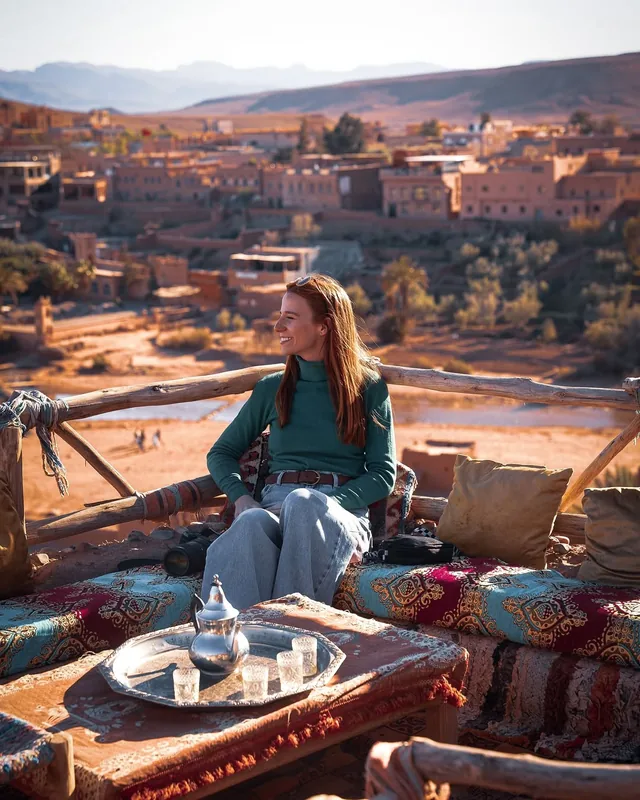 A traveller laughing over a silver tea tray on a terrace facing the Ounila valley village