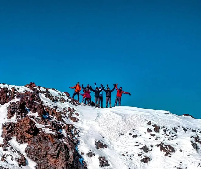 A group of trekkers cheering with arms raised on a snow-covered summit ridge