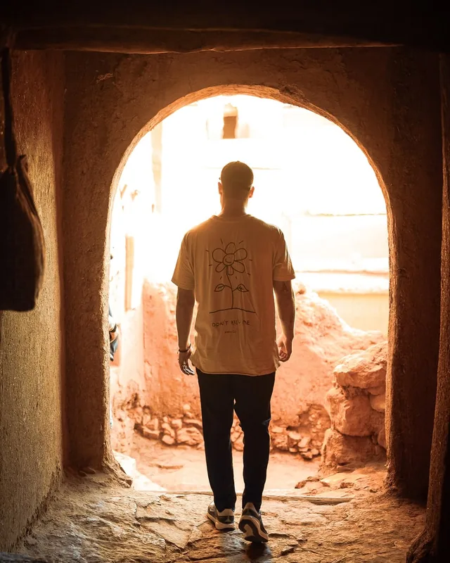 A traveller walking out through a sunlit earthen archway inside the ksar