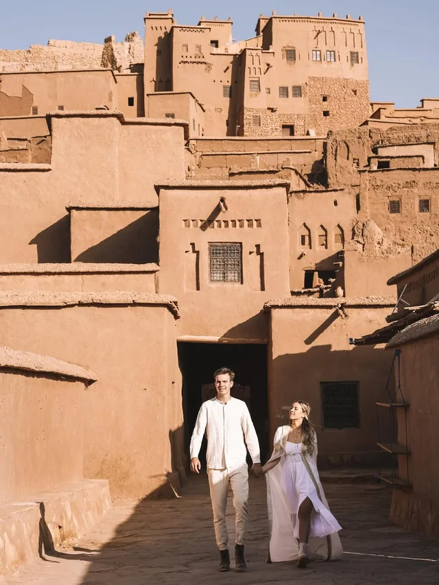 A couple walking out of the shaded gateway beneath the towers of Aït Ben Haddou