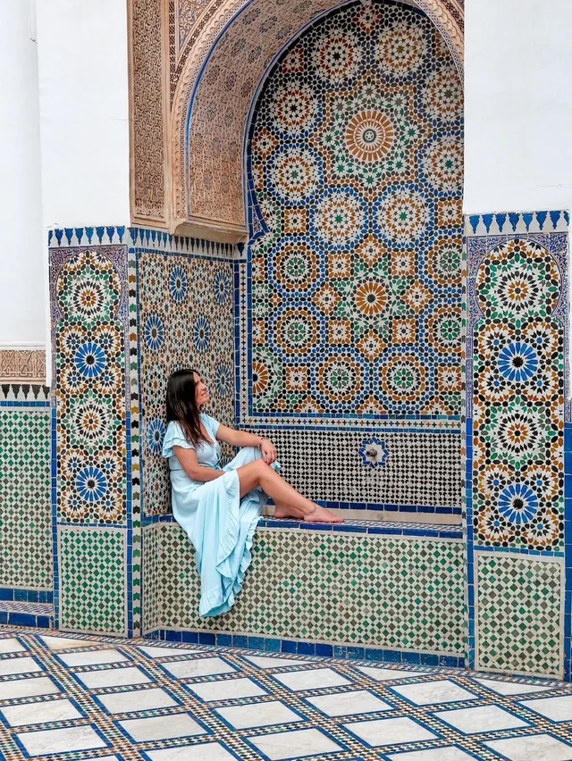A visitor sitting in a zellige-tiled alcove beneath carved stucco in a Marrakech palace